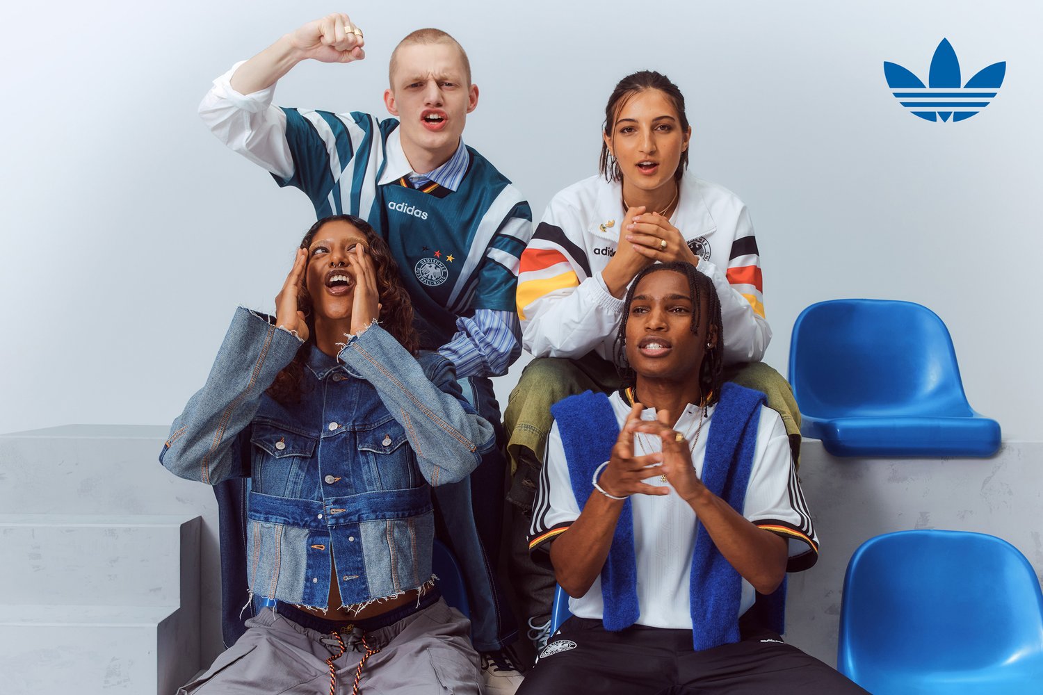 Quattro giovani adulti in abbigliamento sportivo esprimono entusiasmo, con uno che fa il tifo, due che applaudono e uno che urla, seduti in un ambiente informale.