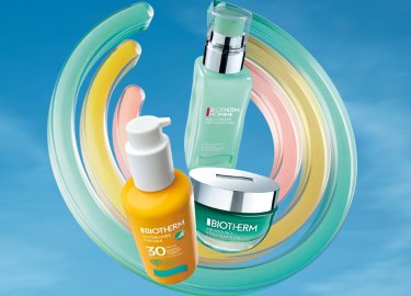 Tres productos de cuidado de la piel de Biotherm están dispuestos contra un cielo azul, rodeados de formas coloridas y en espiral. Los productos incluyen un protector solar, un serum y una crema.