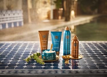 Cinq produits de soin de la peau et des cheveux dans des contenants marron, bleu et cuivre disposés sur une surface carrelée bleue avec un arrière-plan extérieur flou.
