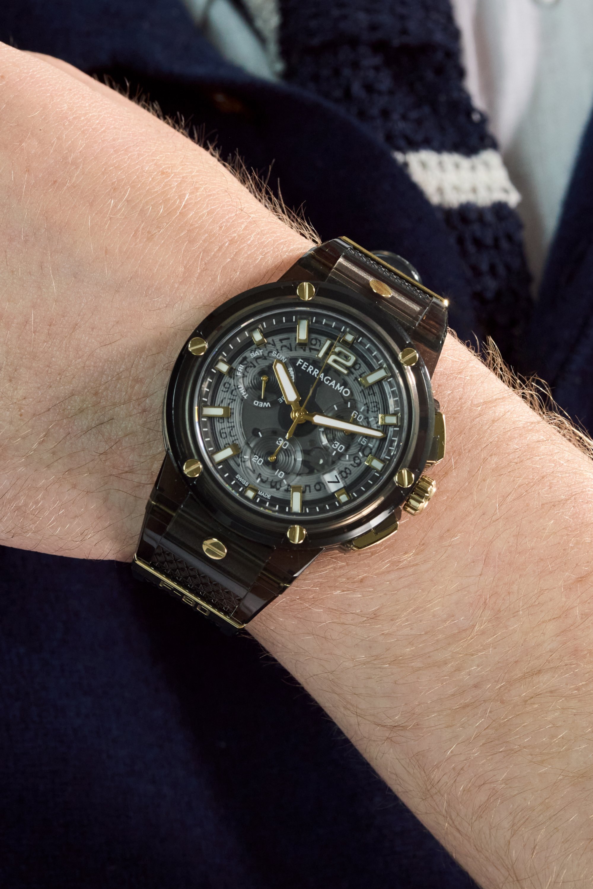 Reloj negro con esfera redonda, acentos dorados y correa texturizada. Presenta múltiples esferas para el día, la fecha y la resistencia al agua.