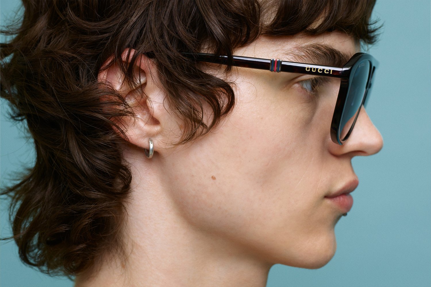 Gafas de sol Gucci con montura negra, lentes oscuros y un logotipo distintivo en las varillas, con sutiles acentos en rojo y verde.