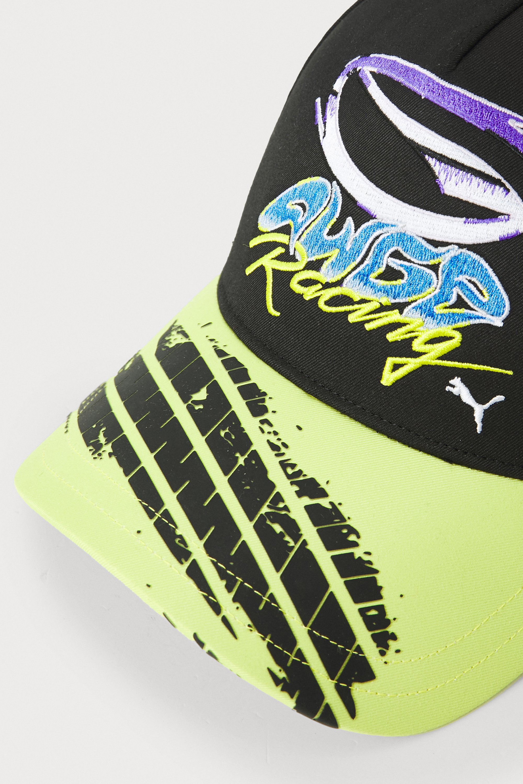 Gorra negra con el vibrante logotipo bordado "Awer Racing" y visera amarilla que presenta un diseño de huella de neumático, enfatizando un tema de carreras.