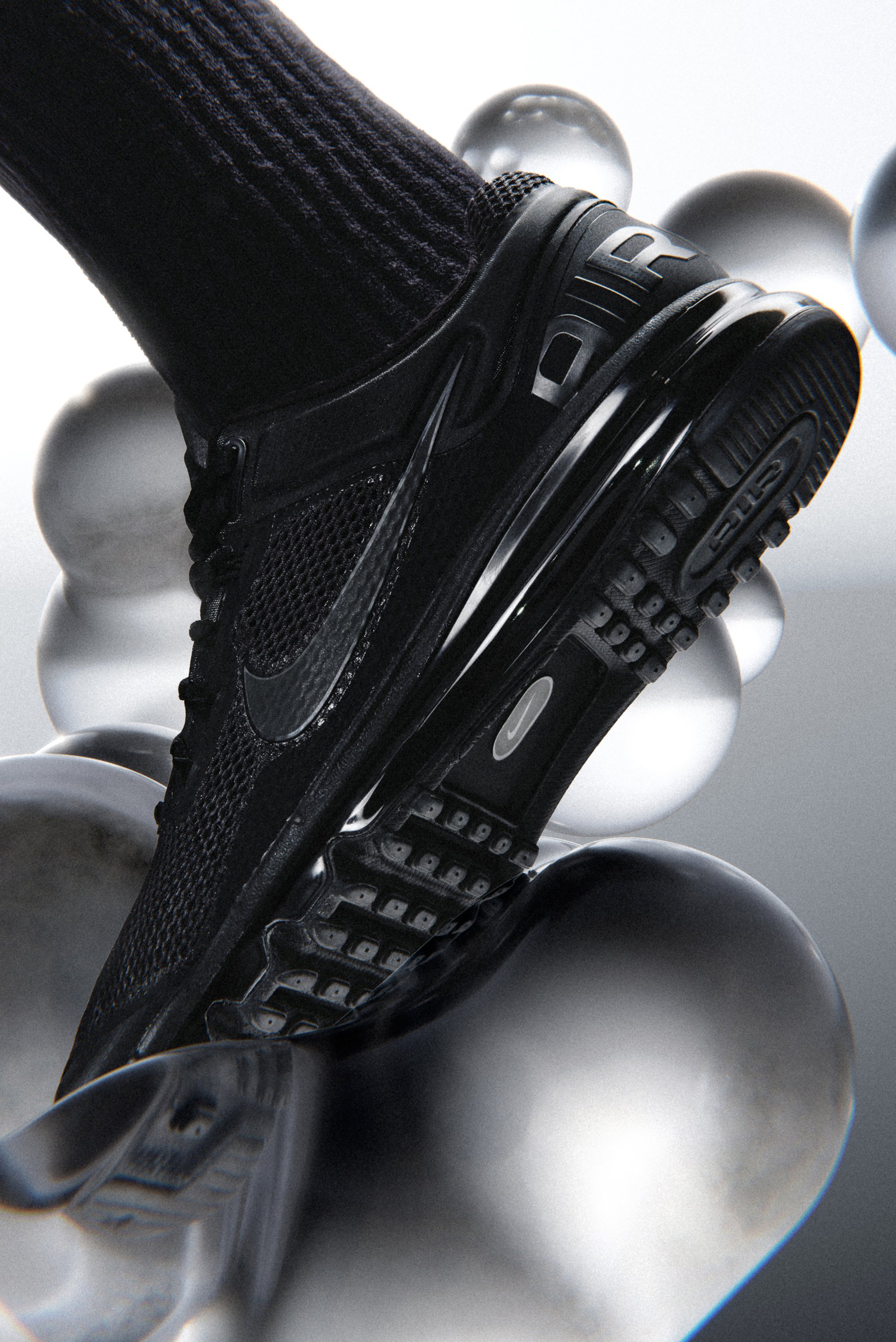 Zwarte Nike sneaker met een gestructureerd bovenwerk en zichtbare luchtzool, gepositioneerd boven glanzende, abstracte bollen tegen een lichte achtergrond.