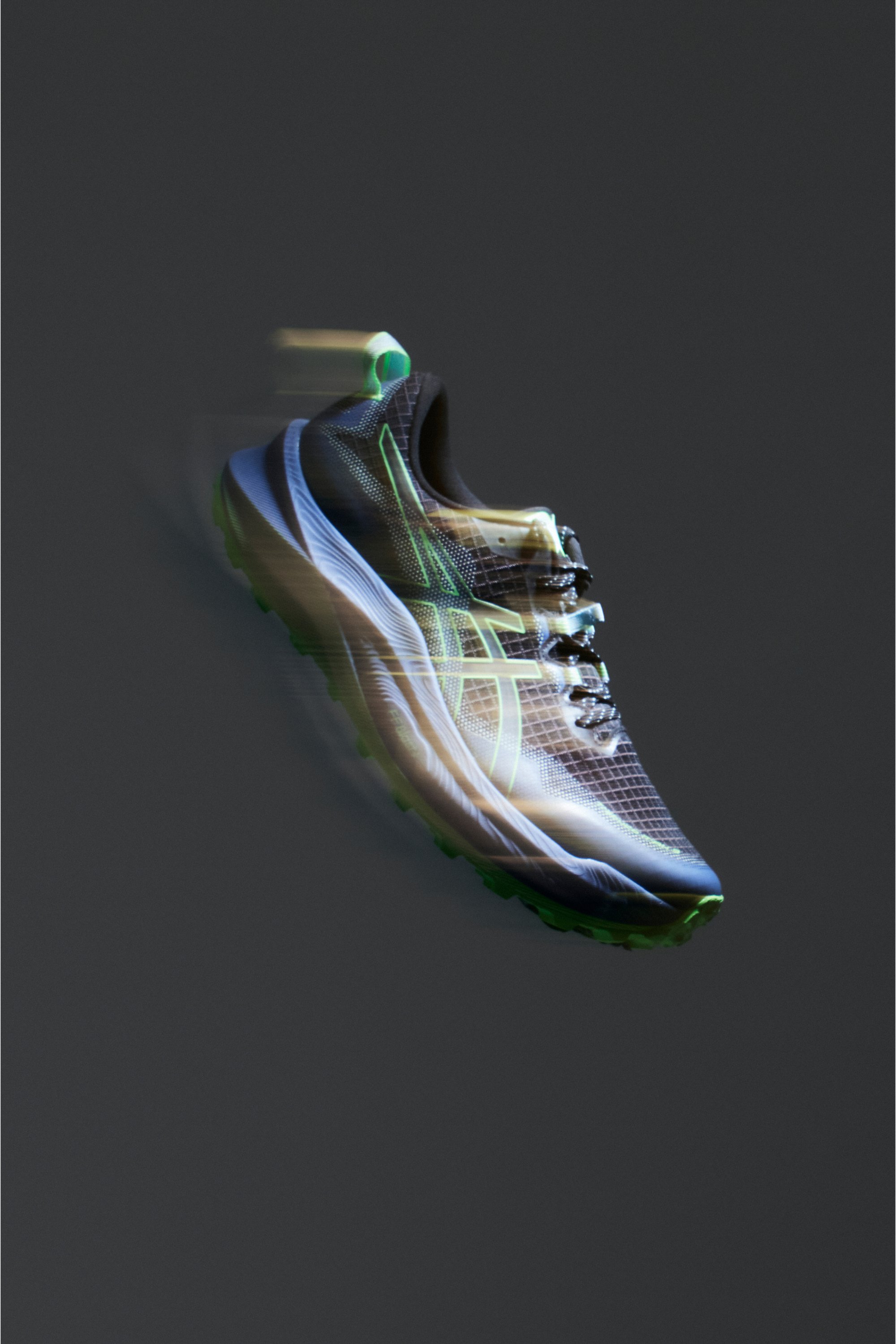 Zapatilla deportiva de running en negro y verde con un efecto de desenfoque dinámico y en movimiento, contra un fondo oscuro.