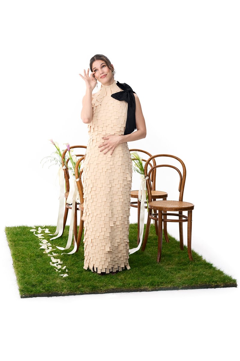 Una bailarina con un vestido púrpura fluido posa sobre un suelo de cuadros en blanco y negro, mientras otra mujer con un vestido beige texturizado se limpia una lágrima.