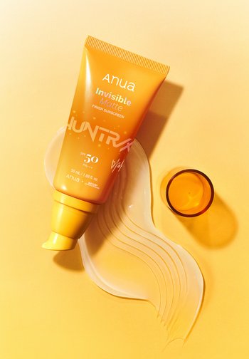 Yellow-orange tube of Anua Invisible Matte sunscreen SPF 50 with clear sunscreen smear and tinted cap on yellow background.