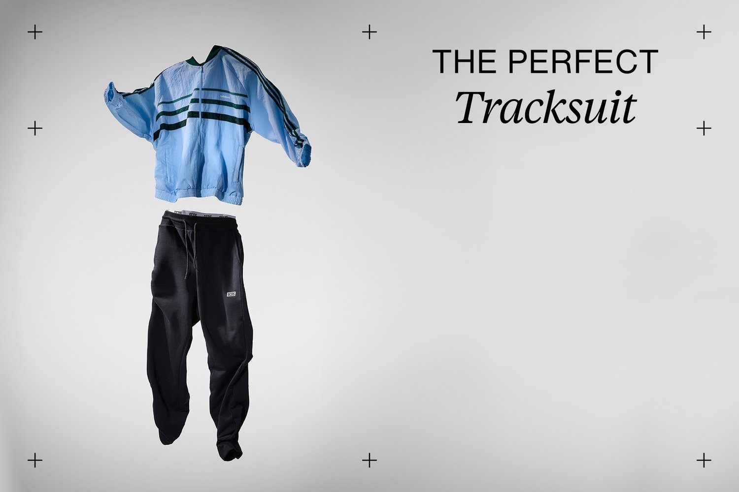 A blue tracksuit top with green stripes is paired with black sweatpants, presented against a minimalistic gray background.