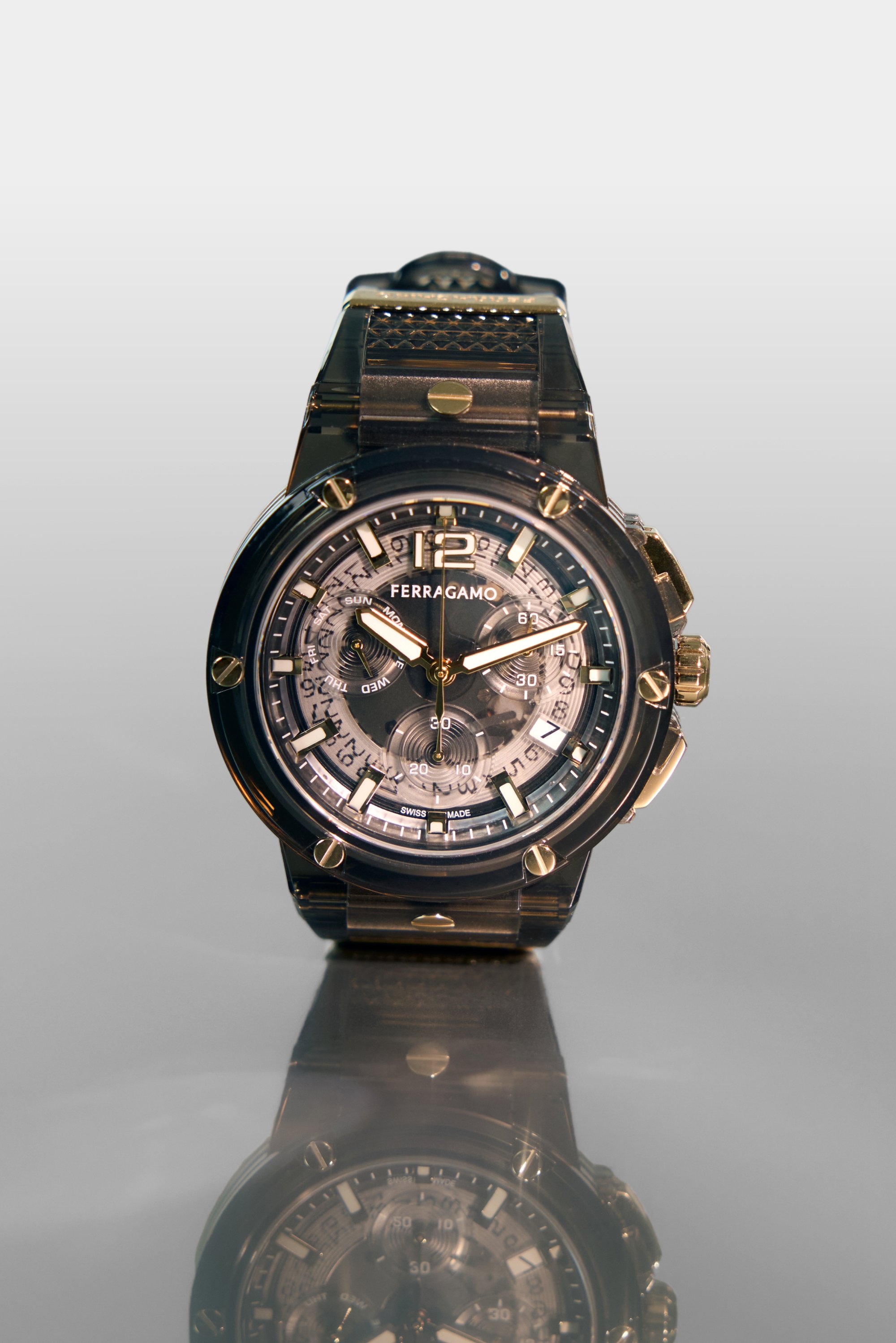 Reloj Ferragamo negro y dorado con un dial texturizado, características de cronógrafo y marcadores luminiscentes. La superficie reflectante resalta el diseño.