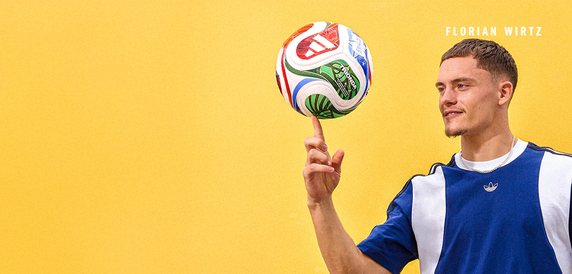 Wielokolorowa piłka nożna wiruje na palcu. Osoba ubrana jest w niebieską i białą koszulkę Adidasa, stojąc przed żółtym tłem.