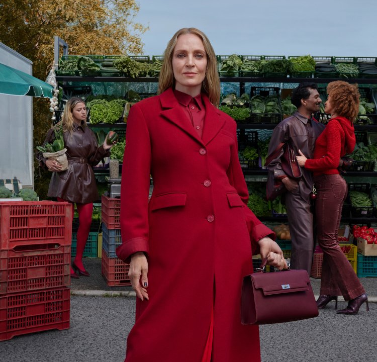 Red coat with a tailored design, coordinating blouse, and handbag. Market scene with green vegetables and crates in the background.