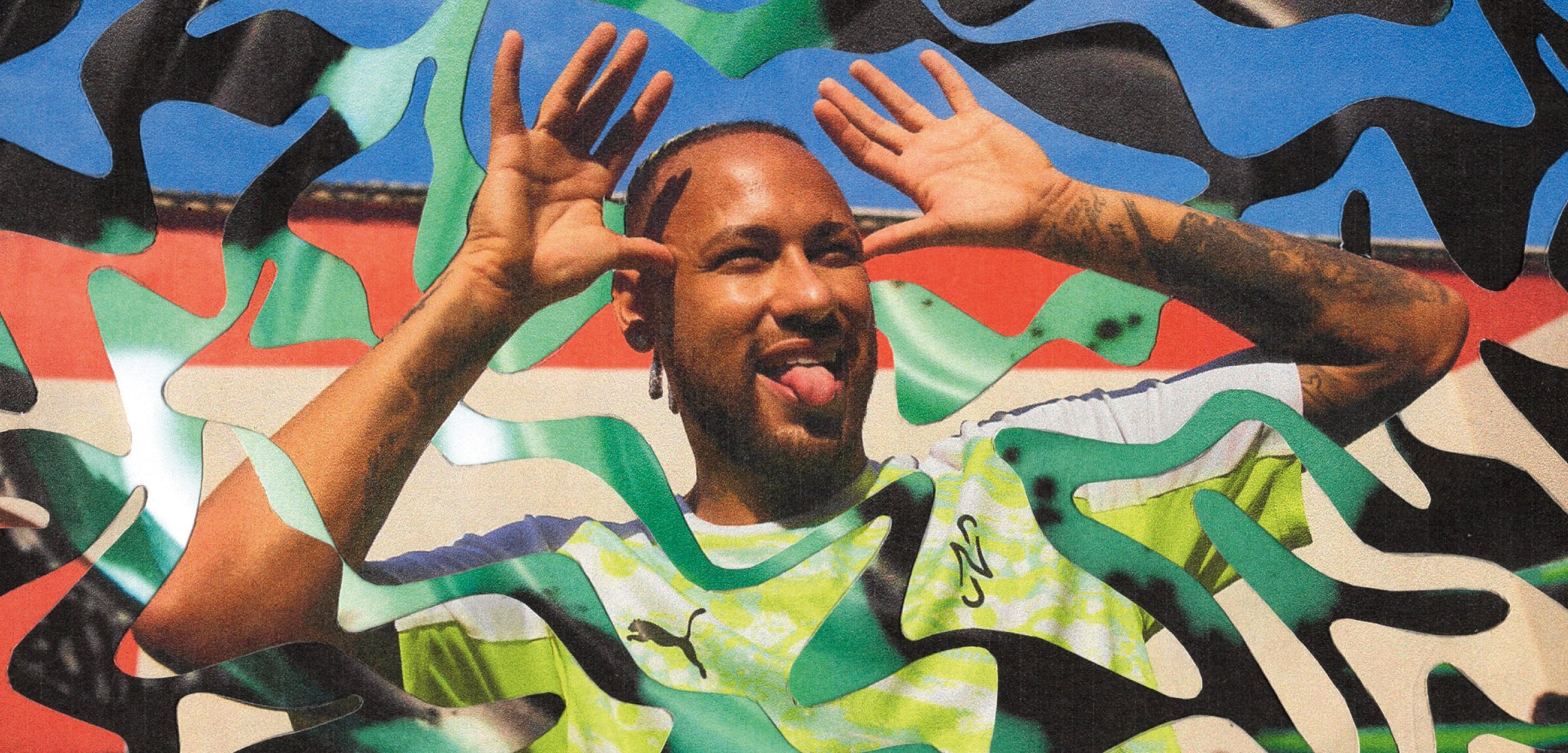 Homme portant un t-shirt Puma vert et blanc faisant une grimace en tirant la langue et levant les mains comme des bois de cerf devant un mur de graffitis coloré.