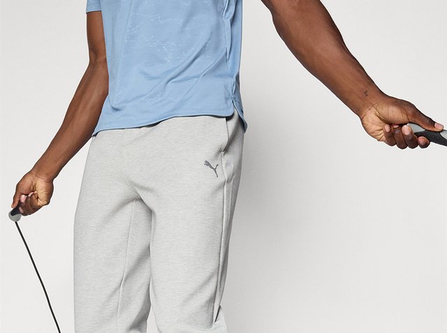 Persoon in een lichtblauw shirt en grijze Puma-sweatpants die springtouwgrepen vasthoudt en zich klaarmaakt om te springen.
