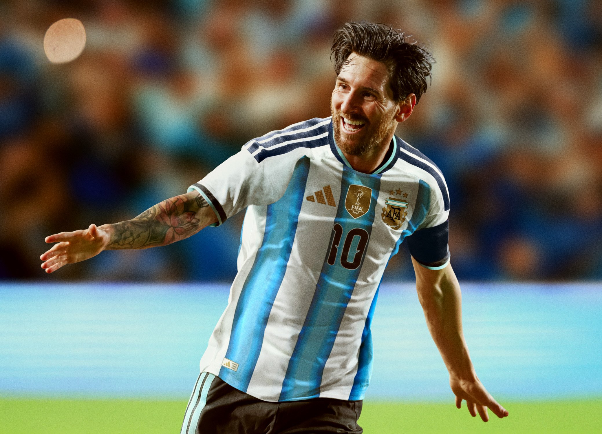 Piłkarz w niebiesko-białej, pasiastym stroju, numer 10, świętujący z rozpostartymi ramionami na rozmytym tle stadionu.