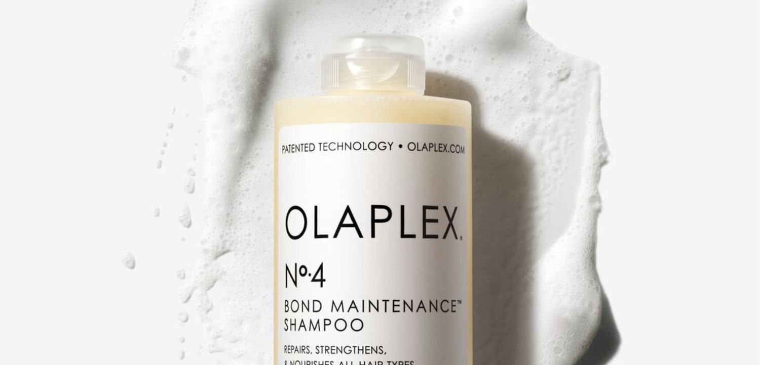 Bottiglia di shampoo Olaplex No. 4 Bond Maintenance circondata da schiuma bianca su una superficie chiara.