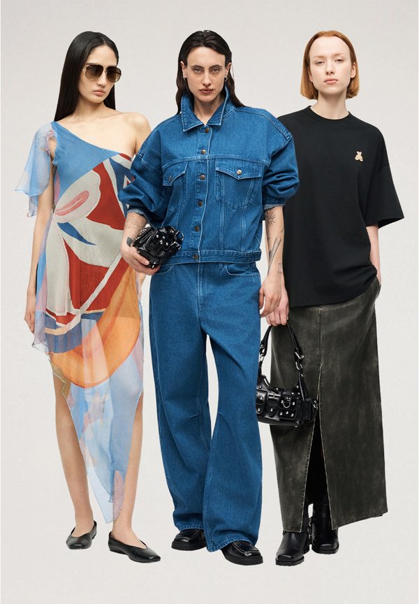 Tres mujeres están de pie una al lado de la otra, una lleva un vestido colorido asimétrico con gafas de sol, otra una chaqueta vaquera y pantalones sujetando una bolsa negra, y la tercera una camiseta negra con una falda larga.