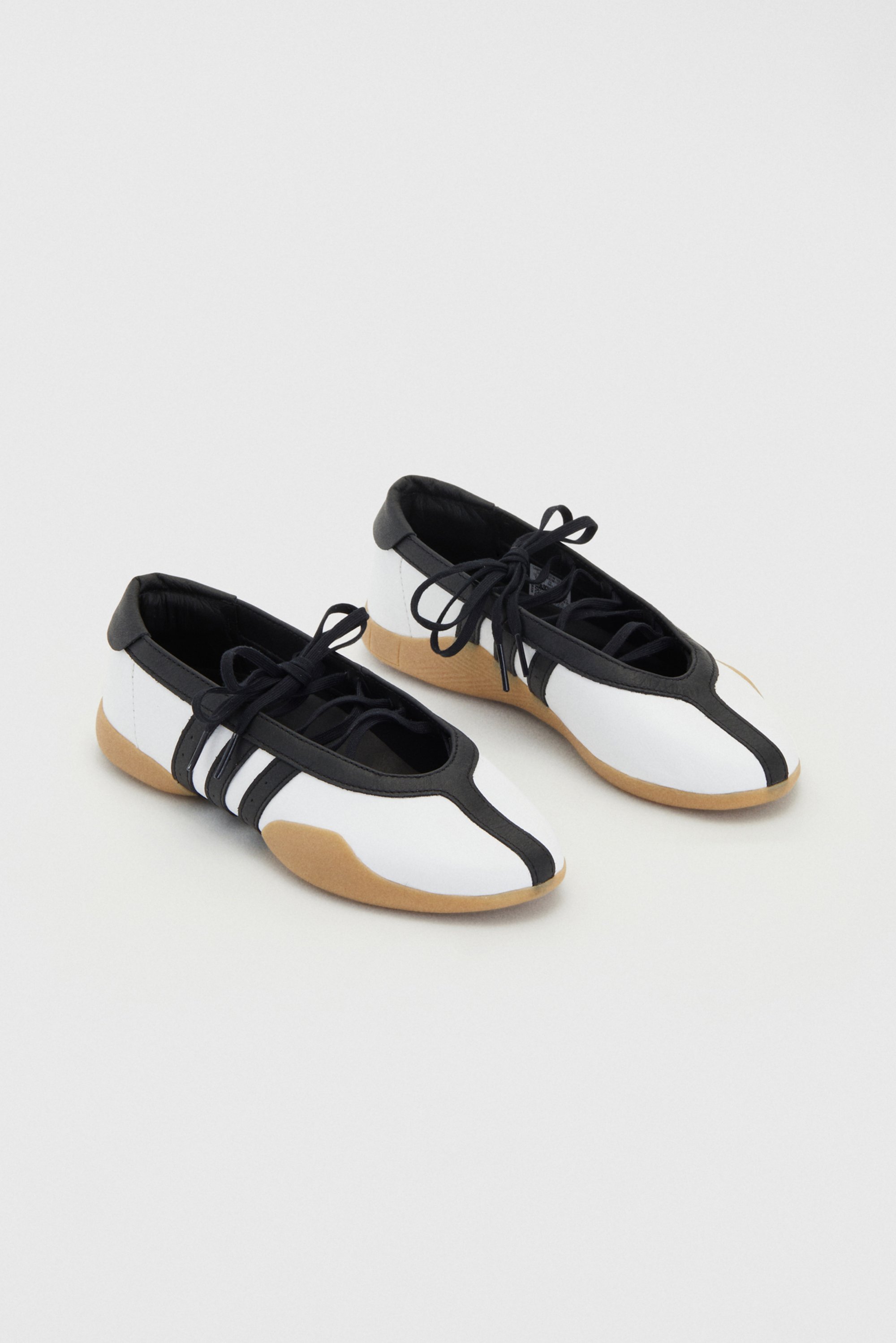 Stylish black and white shoes with a low profile and gum rubber sole, featuring laces and three black stripes on the side.