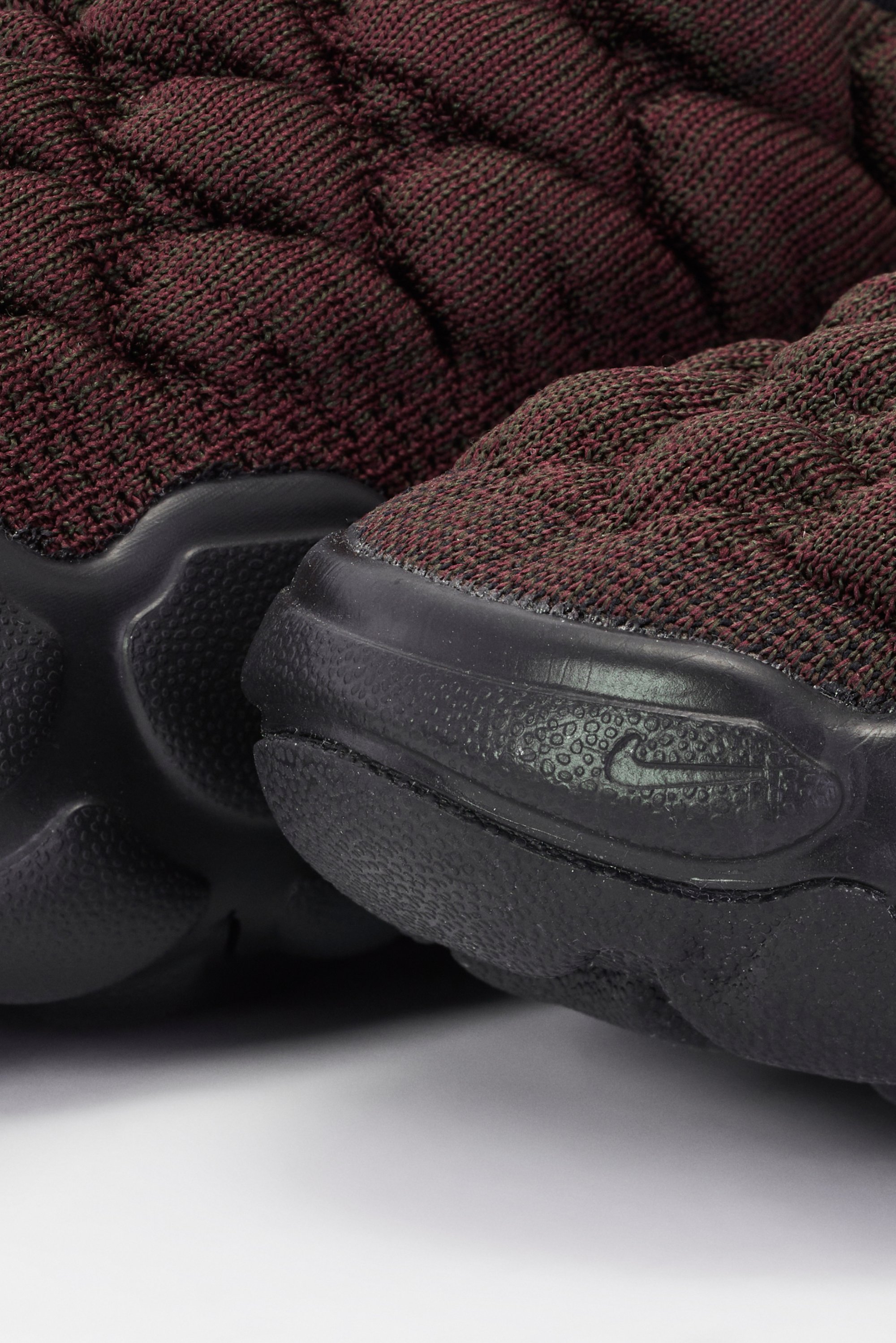 Close-up of burgundy and black textured sneaker, featuring a prominent Nike logo and a cushioned sole design.