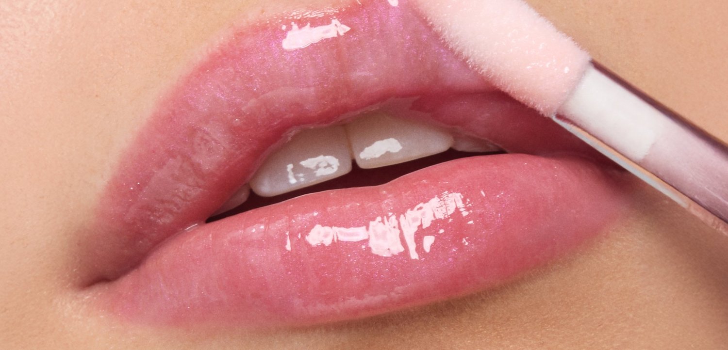 Glänzender rosa Lipgloss, der auf leicht geöffnete Lippen mit sichtbaren oberen Vorderzähnen aufgetragen wird.