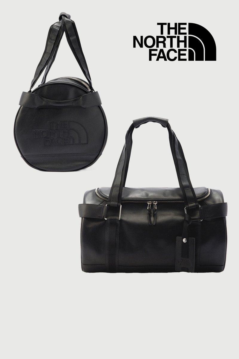 Dos bolsas de viaje negras de North Face, una redonda con correa para el hombro y otra rectangular con asas dobles y parte superior con cremallera, sobre un fondo claro.