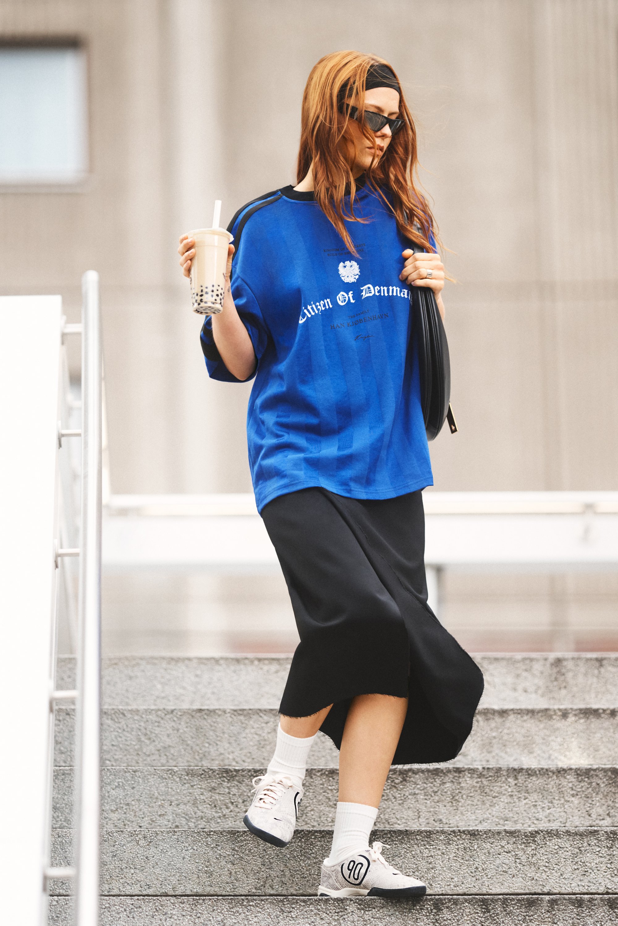 Camiseta azul de gran tamaño con el texto "Ciudadano de Dinamarca", combinada con una falda larga negra y calcetines blancos. Zapatillas beige con detalles en negro.