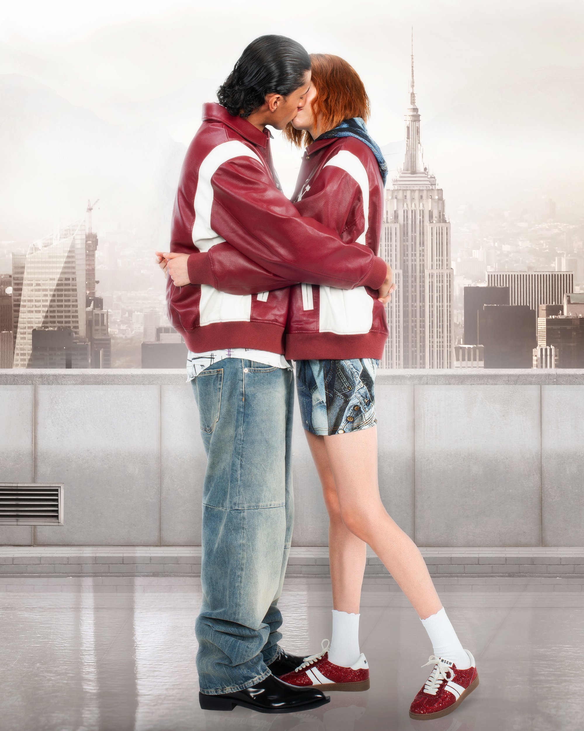 A couple in matching red and white jackets kisses, with the Empire State Building visible in the background against a cityscape.