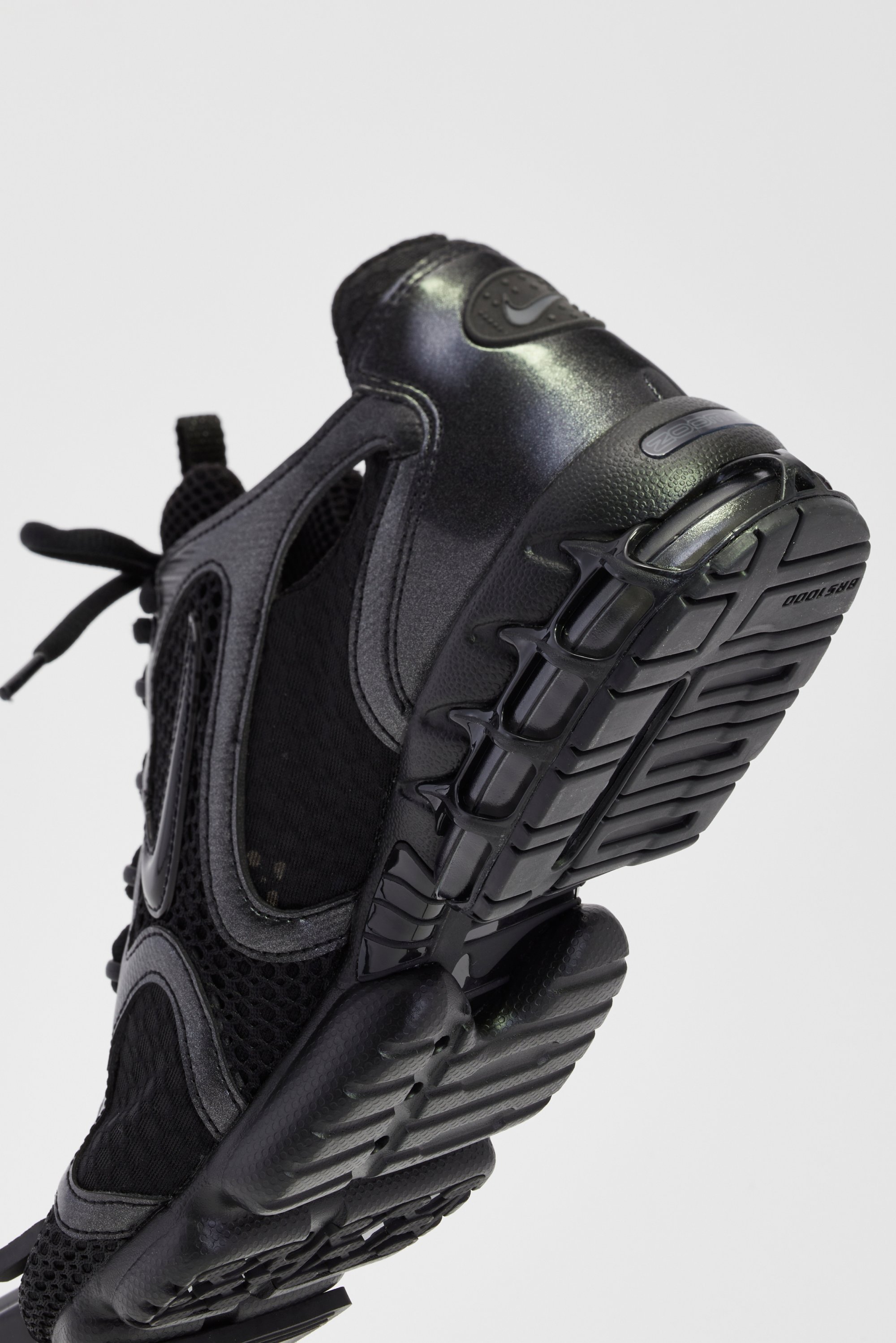 Zwarte sportschoen met een gestructureerde zool en een bovenwerk van mesh, schuin geplaatst om het onderscheidende ontwerp en het Nike-logo te tonen.