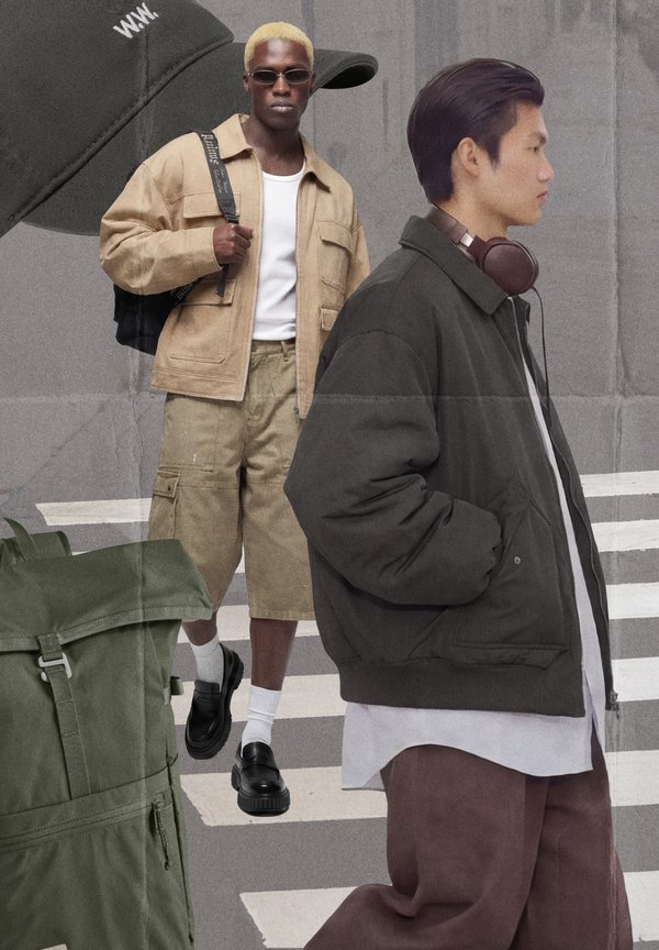 Deux hommes en tenue décontractée de rue : l'un en short beige avec une veste, des lunettes de soleil et un sac à dos, l'autre en veste foncée avec des écouteurs, traversant une rue.