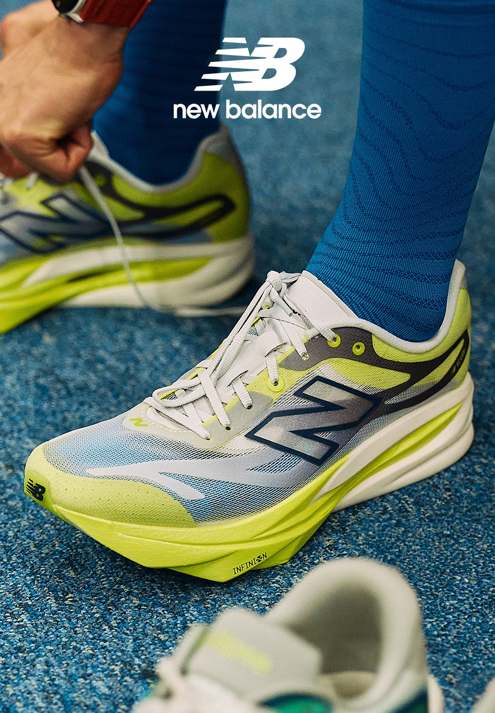 Personne attachant des chaussures de course New Balance jaune néon et grises avec des chaussettes bleues sur un sol moquetté bleu, montrant le logo de la marque au-dessus.