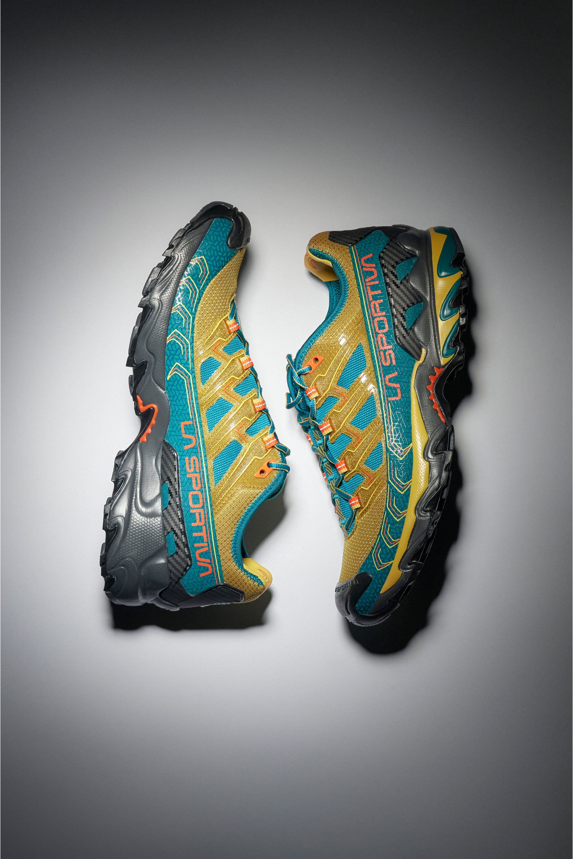 Zapatillas de trail running brillantes en amarillo y azul, con suelas texturizadas, cordones y logotipos, exhibidas sobre un fondo neutro.