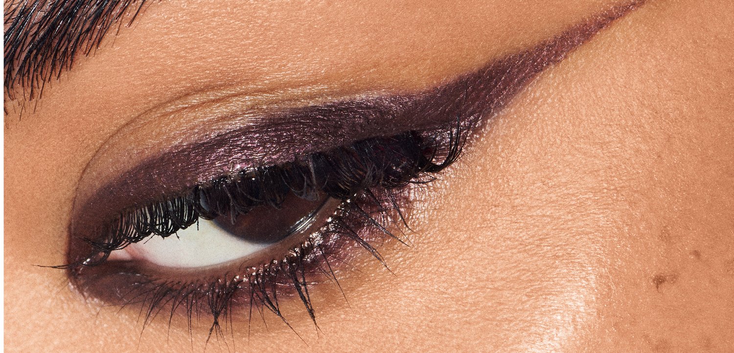 Gros plan sur un œil avec un fard à paupières violet profond, un eyeliner bien défini et de longs cils noirs, le tout sur un teint de peau lisse et clair.