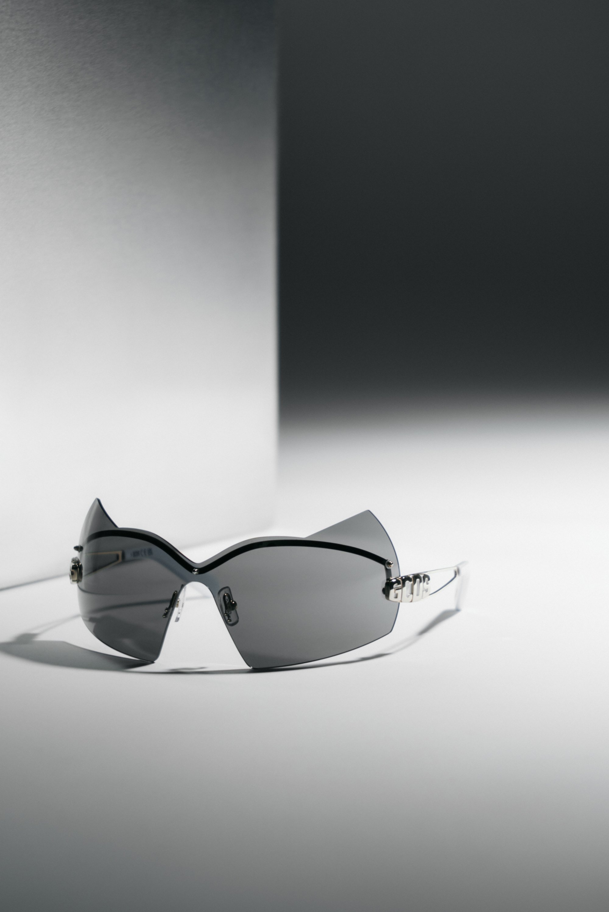 Gafas de sol negras y elegantes con un diseño angular, que cuentan con lentes tintados y adornos decorativos en los lados, colocadas sobre un fondo degradado.