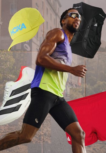 Mężczyzna biegacz w okularach przeciwsłonecznych i sportowym ubraniu, unosząca się żółta czapka, czarna kamizelka, białe buty do biegania i czerwone szorty na tle ulicy miejskiej.