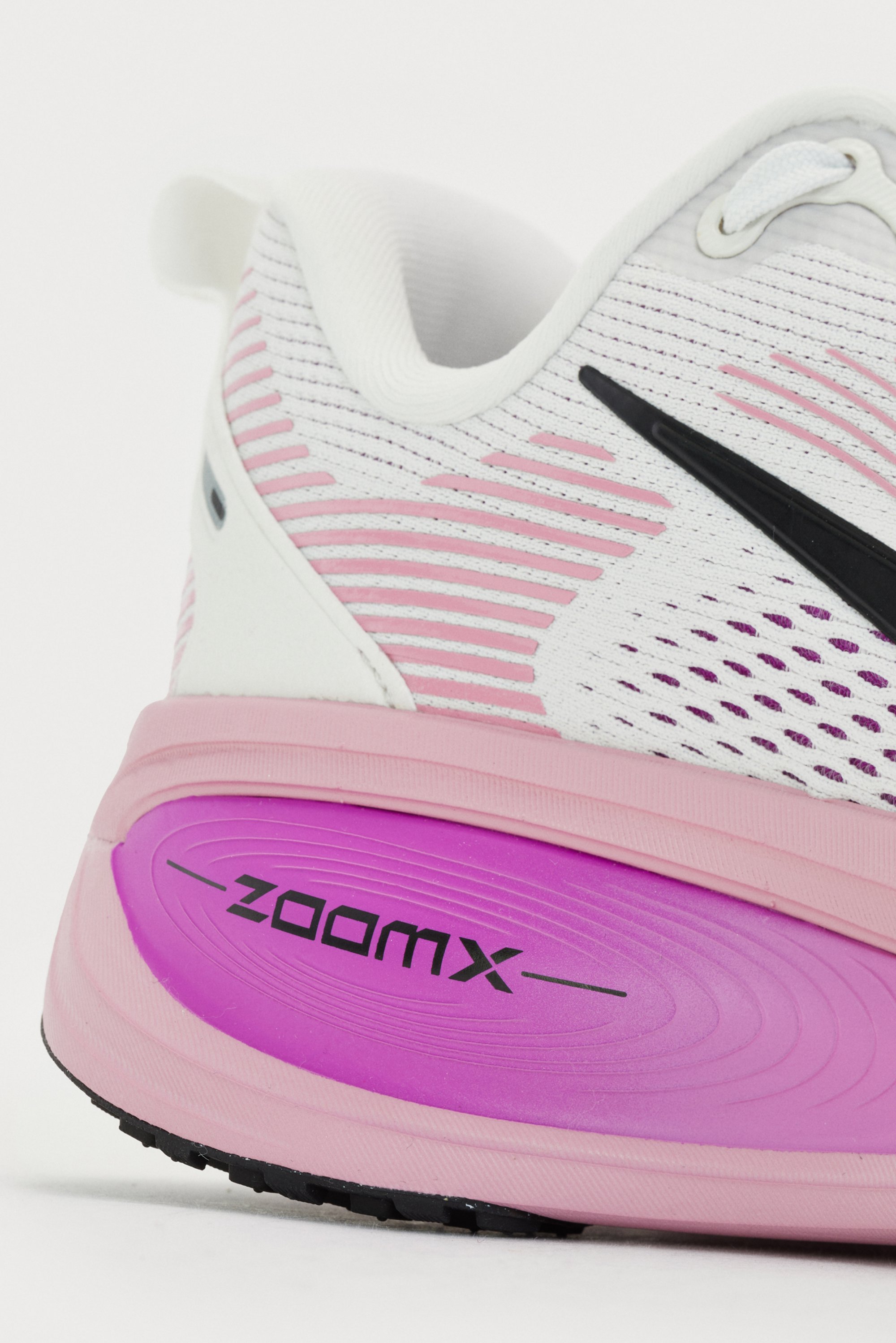 Primer plano de una zapatilla deportiva blanca y rosa con una parte superior texturizada y una media suela rosa pronunciada con la marca "ZOOMX" en el costado.