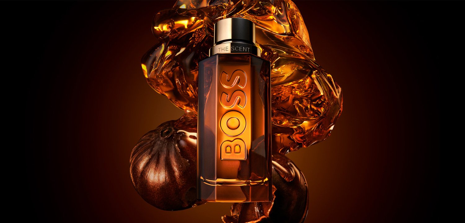 Brun glas parfume flaske mærket Boss The Scent med abstrakte ravvæskeformer og mørke runde frugter i baggrunden.