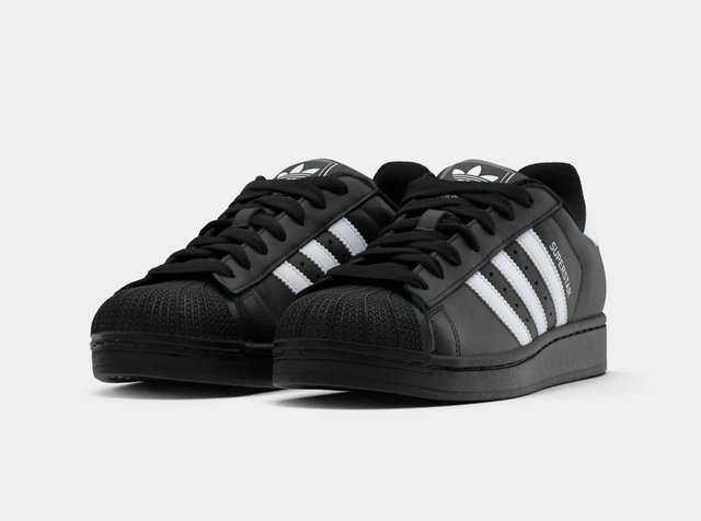 Paire de baskets Adidas Superstar noires avec des bandes blanches et des lacets noirs sur un fond blanc uni.