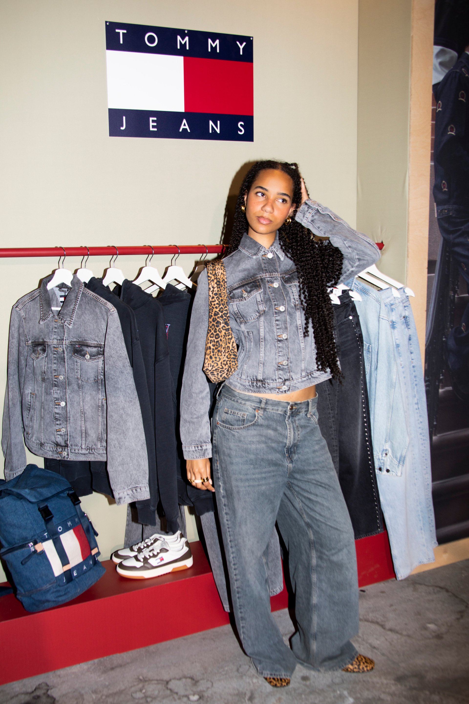 Denim jacket in lichtgrijs met knoopsluiting, gecombineerd met grijze broek met wijde pijpen. Handtas met luipaardprint en blauwe rugzak liggen dichtbij.