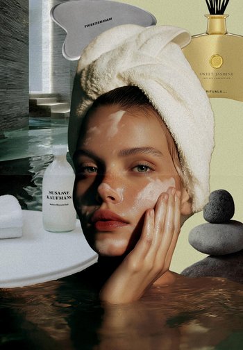 Scena zabiegu na twarz z osobą mającą na głowie biały ręcznik, promienną skórę i delikatnie nakładającą produkt; w tle znajdują się przedmioty do kąpieli i kamienie.