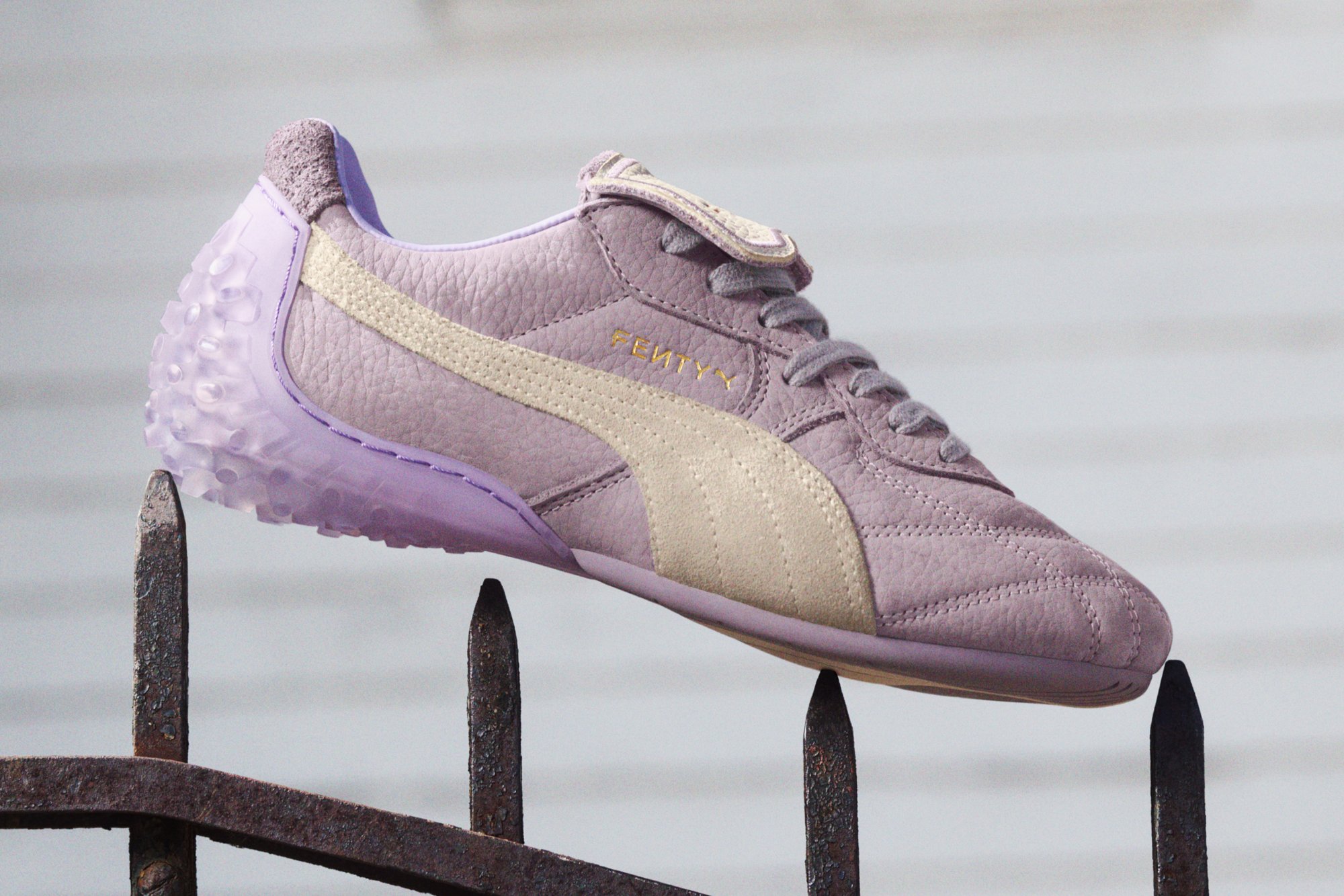 Zapatilla de cuero morada con un acabado texturizado, que presenta una franja de ante beige y una suela translúcida lavanda. Logotipo dorado en el lateral.