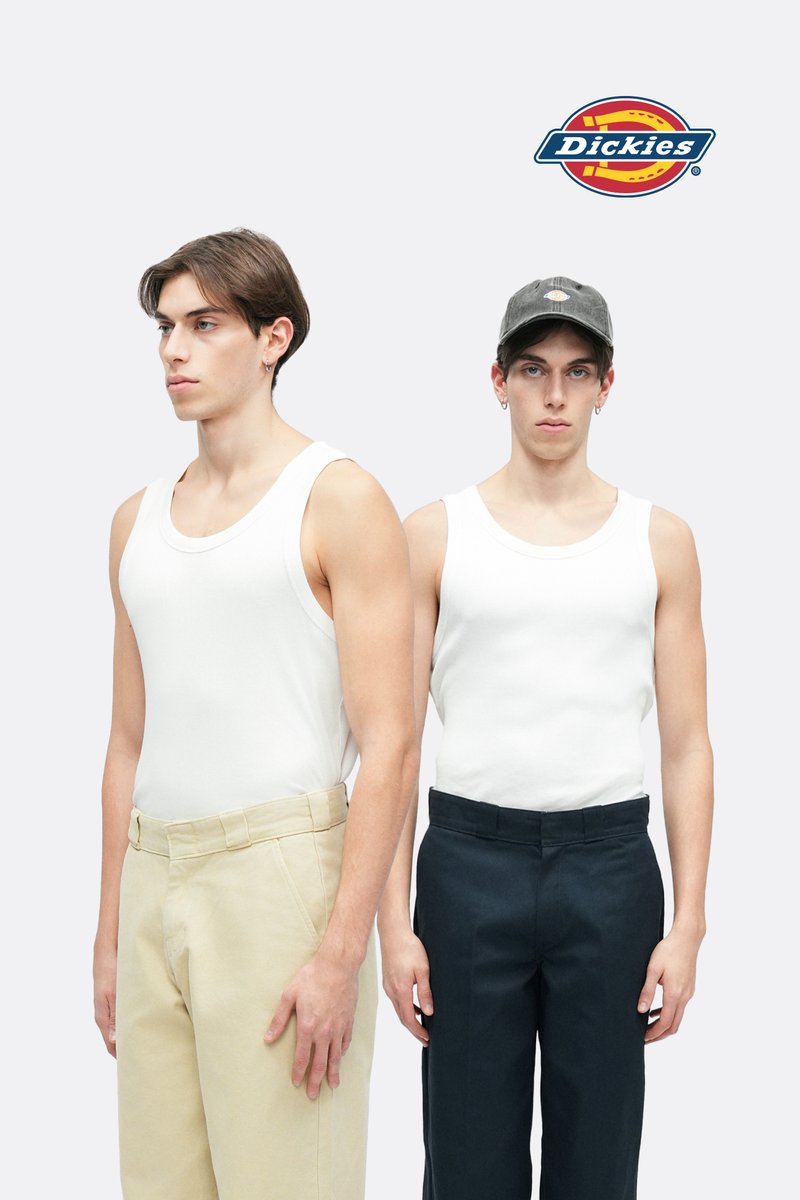 To personer står side om side. Begge bærer hvide tanktoppe. Personen til venstre har lyse beige bukser, personen til højre har mørkeblå bukser.