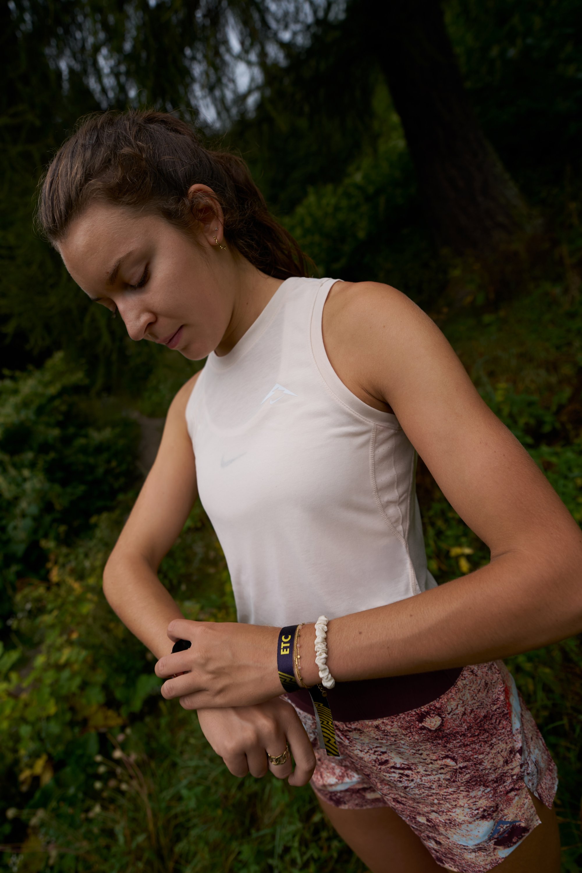 Light pink sleeveless athletic top featuring a logo, patterned shorts in earthy tones, and accessories including a bracelet and a watch.