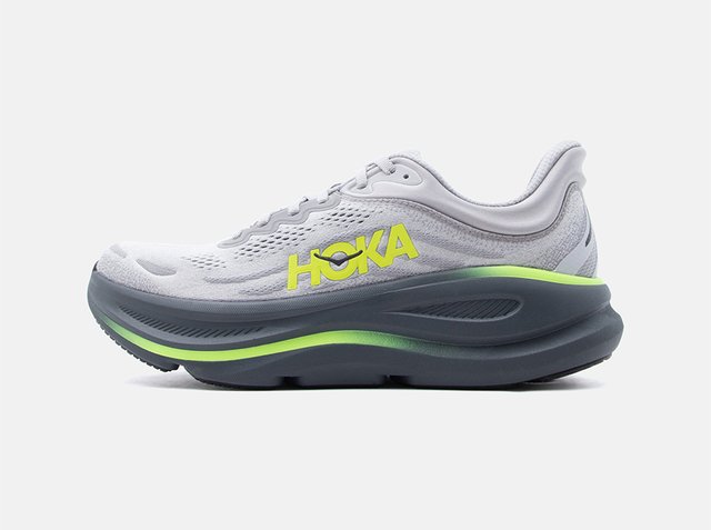 Scarpa da corsa Hoka bianca e grigia con logo giallo neon e suola spessa e ammortizzata progettata per comfort e supporto.