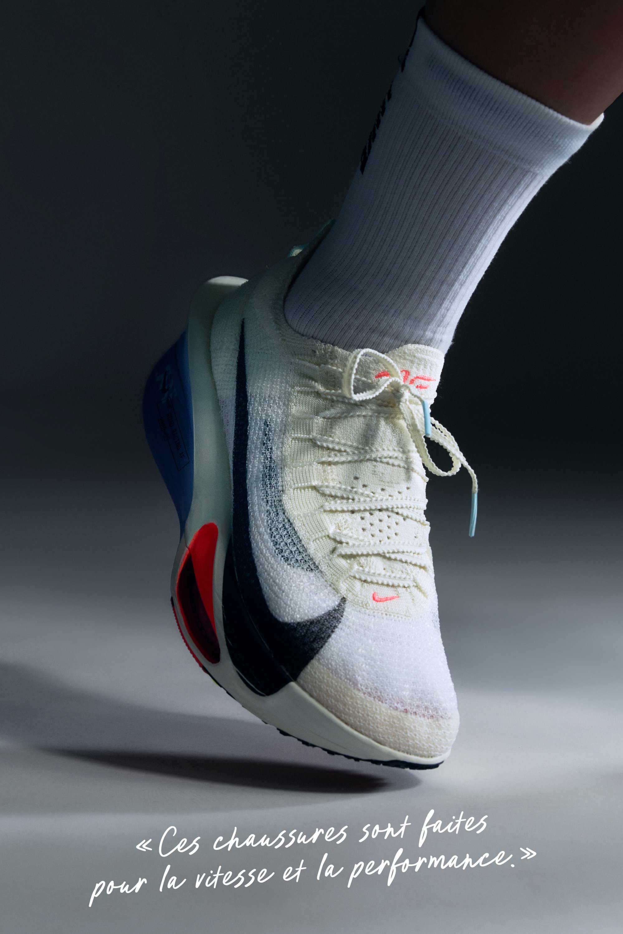 Chaussure de course Nike en crème clair avec un swoosh noir et des accents rouges, présentant un dessus texturé, un design à lacets et une semelle rembourrée.
