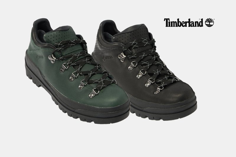 Ein Paar Timberland-Wanderschuhe, einer dunkelgrün und einer schwarz, mit dicken Sohlen und schwarzen Schnürsenkeln vor weißem Hintergrund.