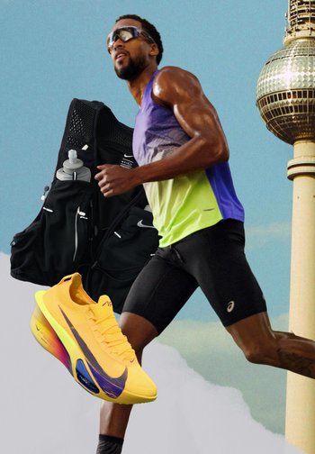 Atleet loopt in een paarse en gele tanktop en zwarte korte broek, met grote gele loopschoenen, een zwarte hydratatievest en de Berlijnse TV-toren op de achtergrond.