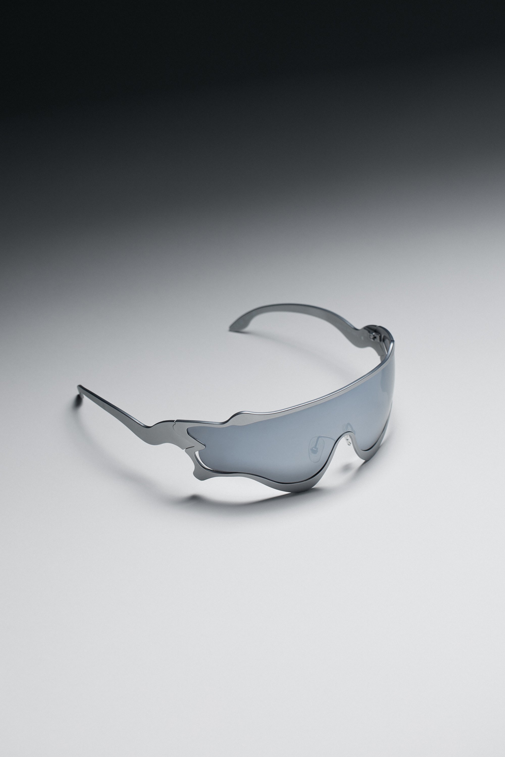Sunglasses with metallic flame-shaped frames and dark lenses rest on a light gradient background, emphasizing their sleek design.