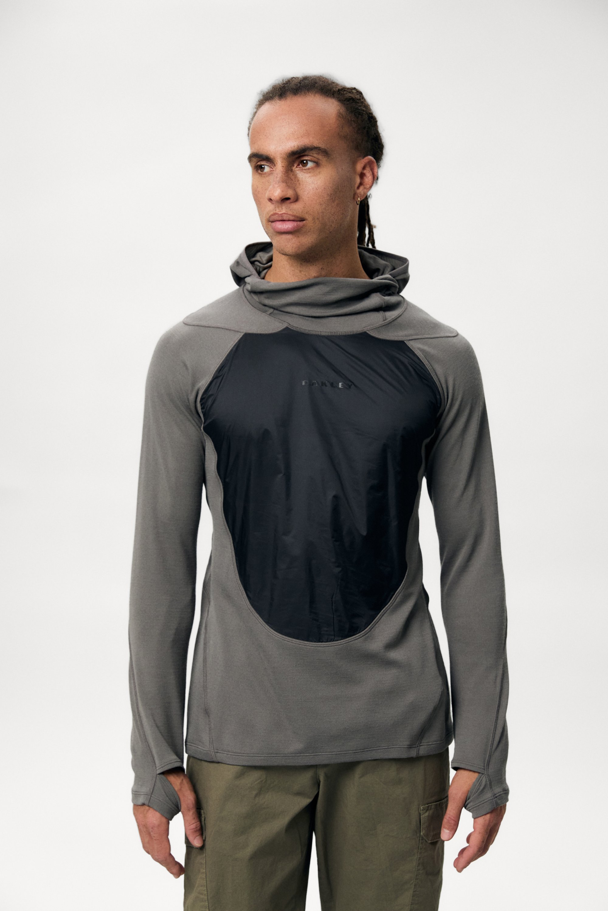 A man with dreadlocks wears a grey long-sleeve shirt featuring a black front panel, set against a plain white background.