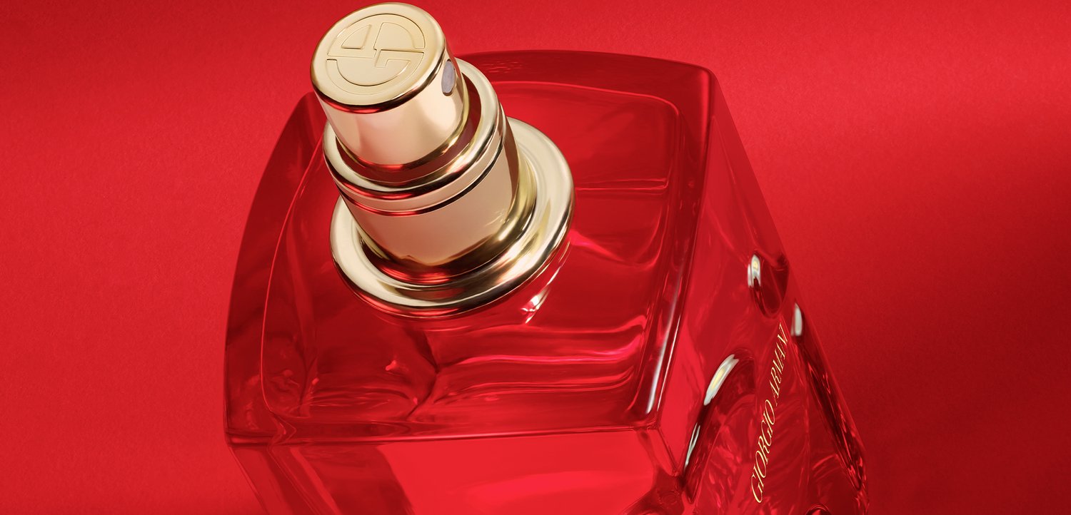 Square transparent glass perfume bottle with gold spray nozzle against a red background.