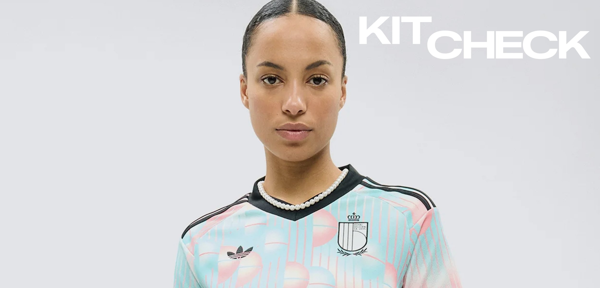 Femme aux cheveux tirés en arrière portant un maillot de sport bleu clair et rose avec des bordures noires et des logos, debout devant un fond clair uni.