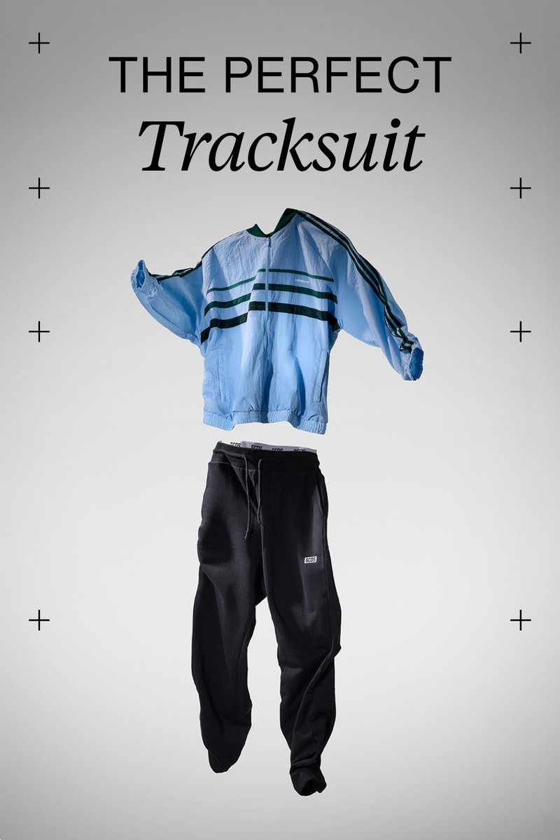 A blue tracksuit top with green stripes is paired with black sweatpants, presented against a minimalistic gray background.