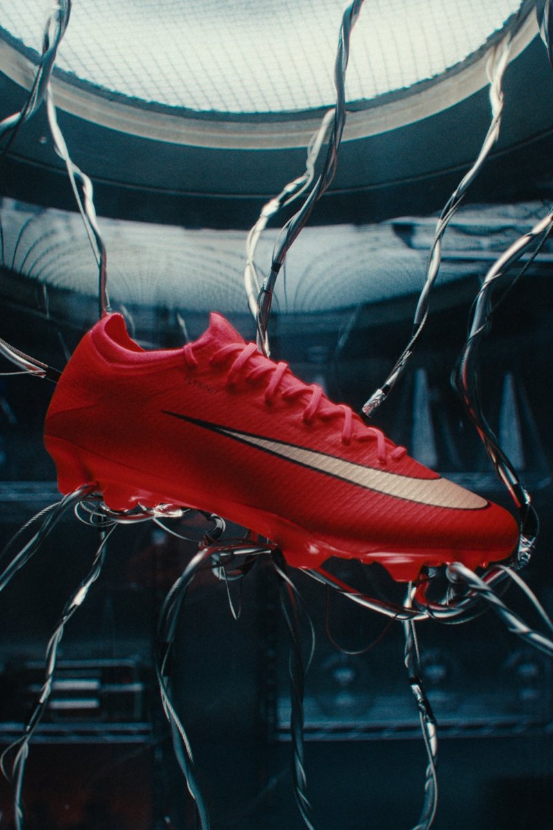 Roter Fußballschuh mit weißem Nike-Swoosh, der an Drähten in einem dunklen, hochmodernen Umfeld hängt.
